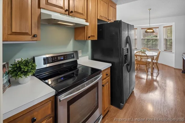 a kitchen with granite countertop a refrigerator a stove a sink dishwasher and wooden cabinets with wooden floor