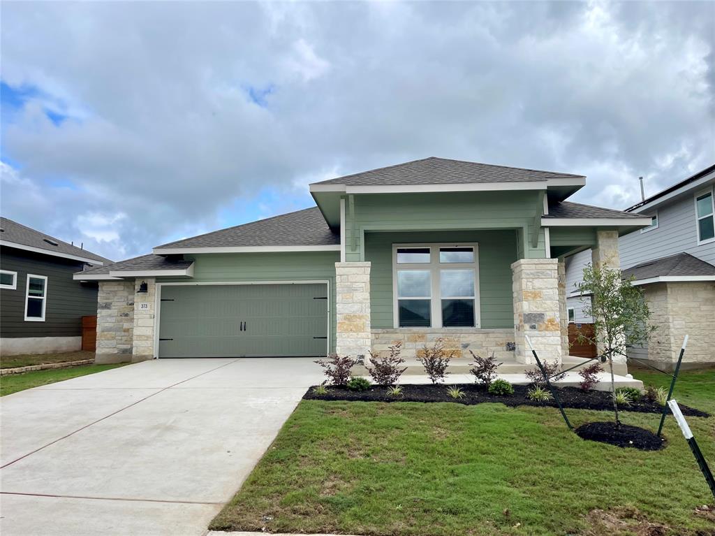 Prairie-style home with a garage, a shingled roof, stone siding, and a front lawn