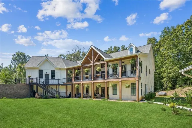 a view of a white house with a big yard and potted plants and large trees