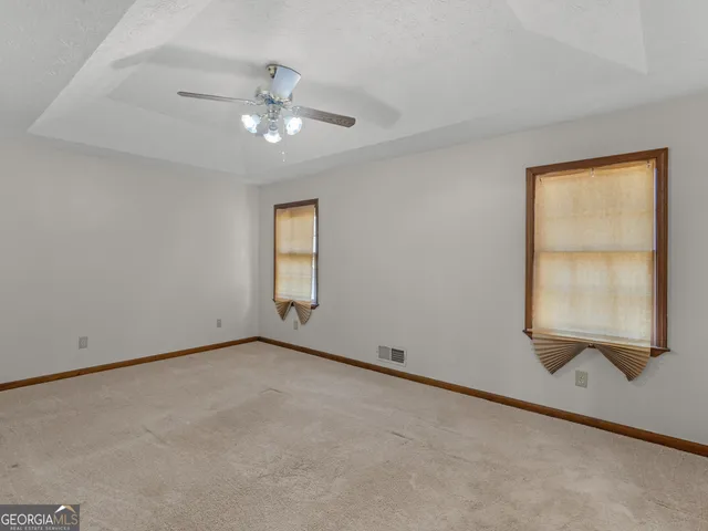 an empty room with a chandelier fan and windows