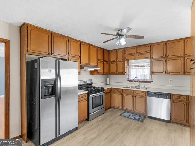 a kitchen with stainless steel appliances granite countertop a refrigerator a sink dishwasher a stove and white countertops with wooden floor