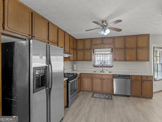 a kitchen with stainless steel appliances granite countertop a refrigerator a sink dishwasher a stove and white countertops with wooden floor