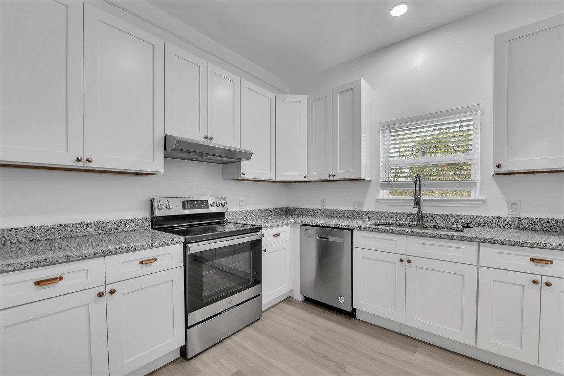 a kitchen with granite countertop stainless steel appliances white cabinets granite counter tops and a wooden floors