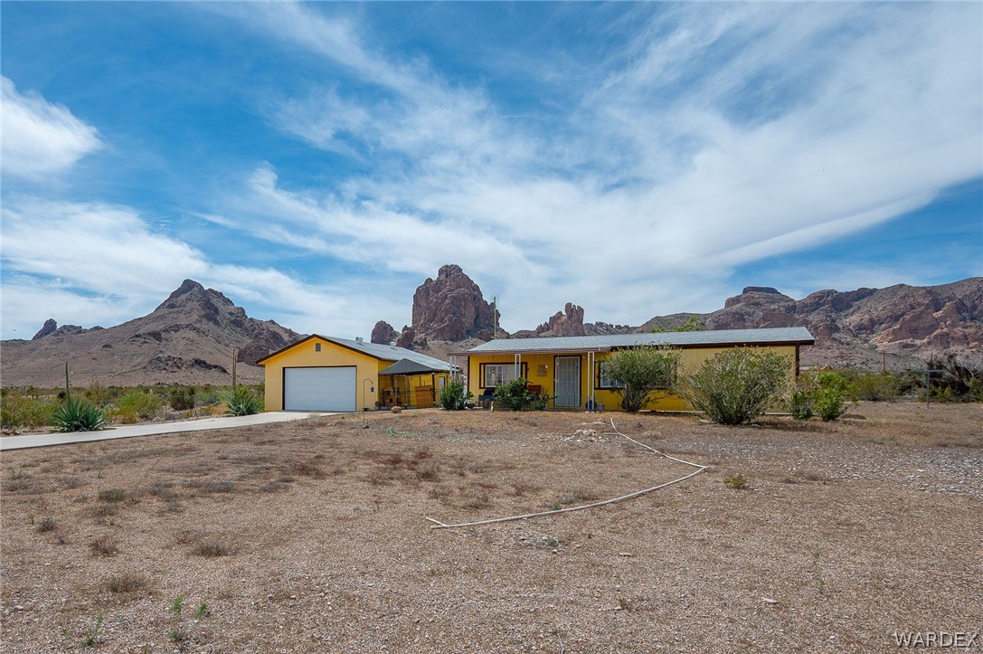 2465 Egar Road Golden Valley, AZ 86413 - Photo 65 of 98 The property features a yellow exterior and an attached garage with a white door, set against a backdrop of prominent rock formations