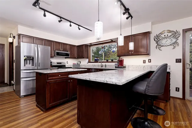 a kitchen with stainless steel appliances granite countertop a refrigerator a sink dishwasher a stove and white countertops with wooden floor