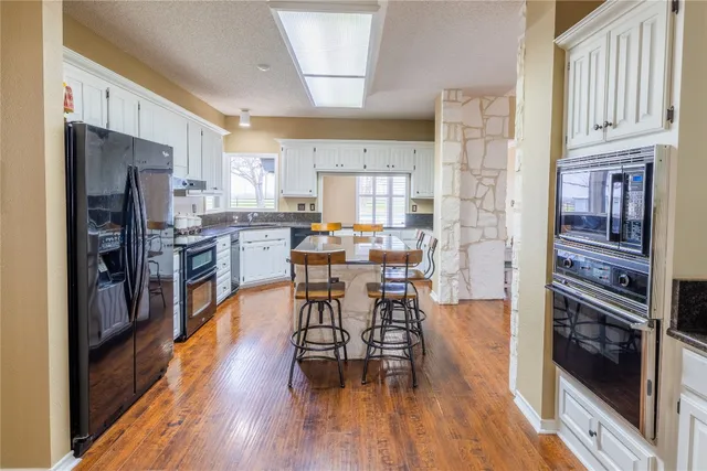 a kitchen with stainless steel appliances granite countertop a stove a refrigerator a sink a dining table and chairs with wooden floor