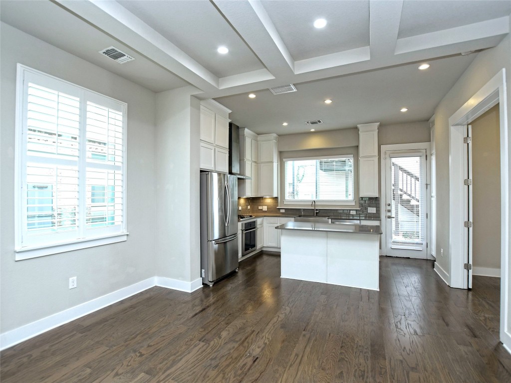 7509 Wildcat Pass Austin, TX 78757 - Photo 14 of 38 Kitchen with backsplash, appliances with stainless steel finishes, a kitchen island, white cabinets, and dark wood-style flooring