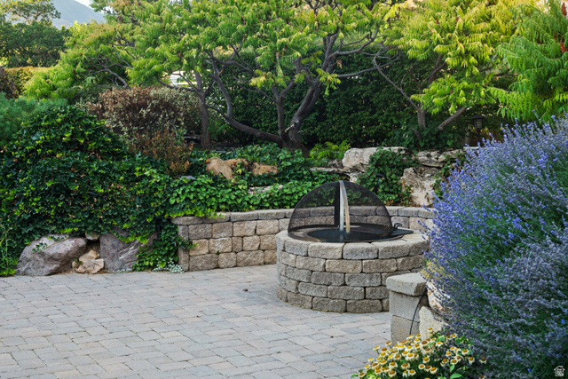 875 South 1250th Street East Mapleton, UT 84664 - Photo 13 of 54 Paved patio featuring a stone fire pit with a mesh cover, surrounded by lush landscaping, mature trees, and a stone retaining wall