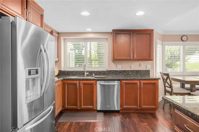 a kitchen with stainless steel appliances granite countertop a refrigerator a sink dishwasher a stove and white countertops with wooden floor