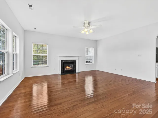 an empty room with wooden floor fireplace and windows