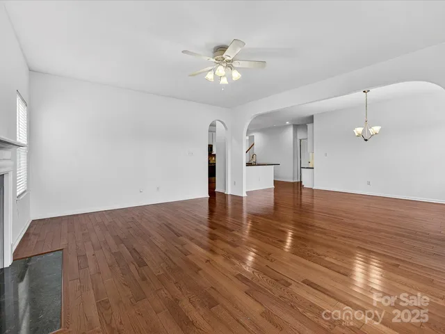a view of an empty room with wooden floor and a ceiling fan