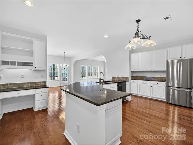 a kitchen with granite countertop a white refrigerator a sink dishwasher a dining table and chairs with wooden floor