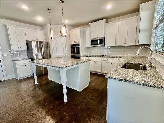 a kitchen with stainless steel appliances granite countertop a sink dishwasher a refrigerator oven a stove with white cabinets and wooden floor