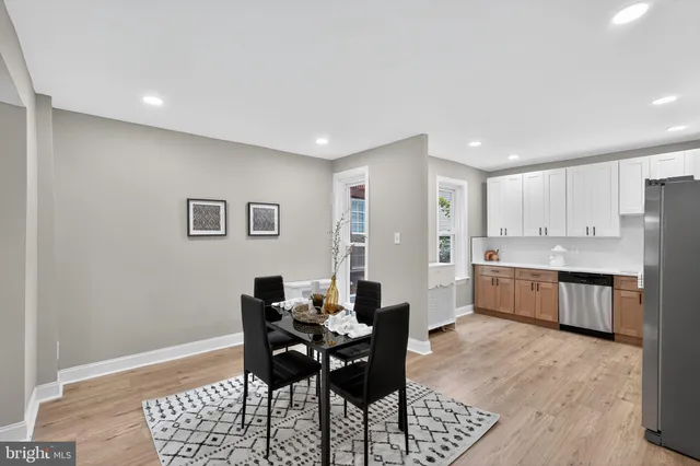 a large white kitchen with granite countertop a dining table chairs and a refrigerator
