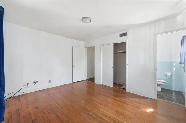 a view of an empty room with wooden floor and a bathroom