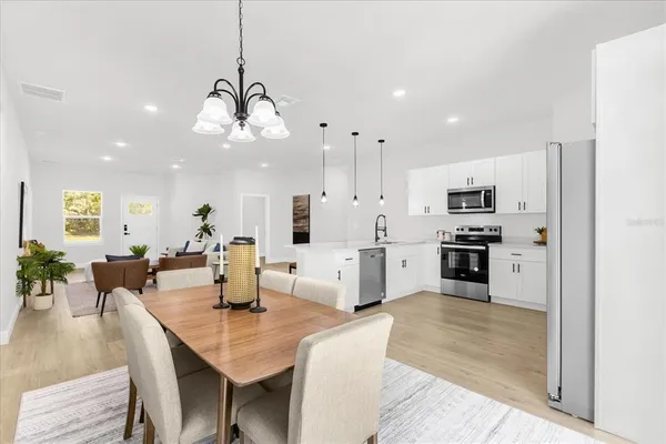 a open kitchen with stainless steel appliances kitchen island granite countertop a refrigerator a stove a sink a dining table and chairs with wooden floor