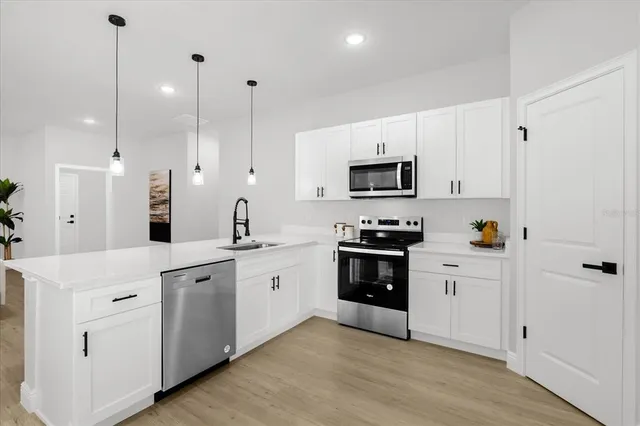 a kitchen with stainless steel appliances white cabinets a sink a stove a microwave and wooden floors