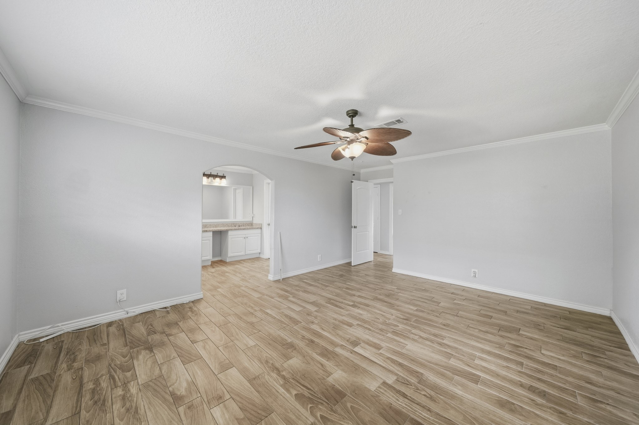 302 Country Road 893 Angleton, TX 77515 - Photo 20 of 26 This room features a spacious area with light wood flooring, a ceiling fan, and neutral-colored walls. It has an open doorway leading to what appears to be a kitchen or dining area with cabinets and a countertop, creating a seamless flow between spaces.