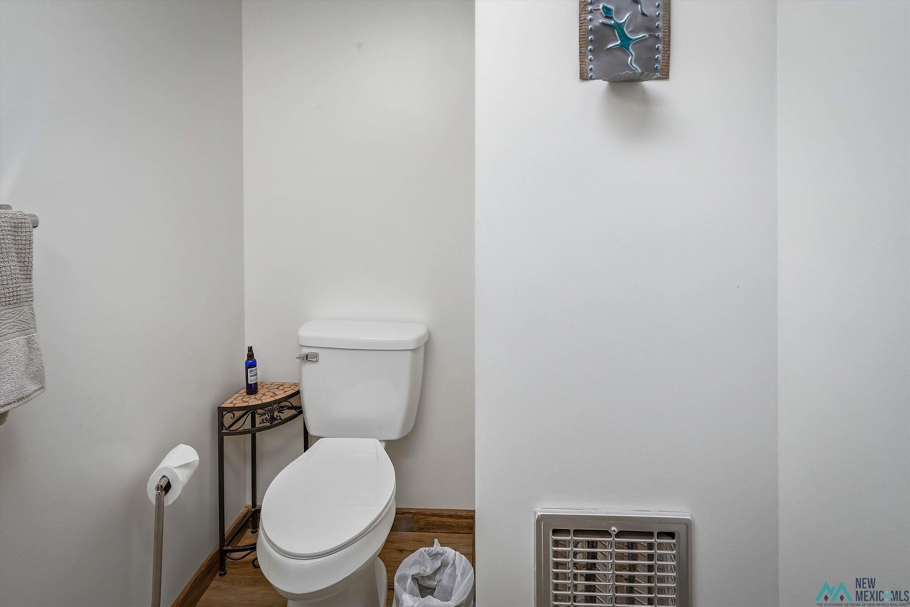 83 Juniper Road Chama, NM 87520 - Photo 21 of 56 White commode with a ceramic tank and bowl, wood-finish flooring, and a metal floor register