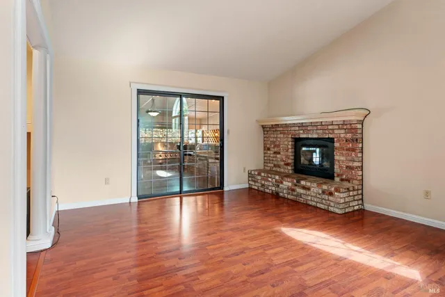 an empty room with wooden floor fireplace and windows