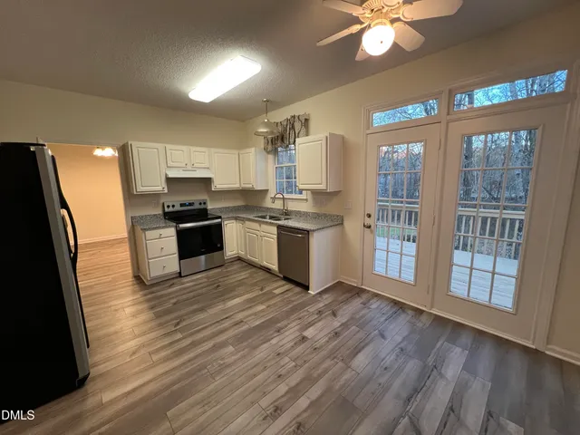 a kitchen with stainless steel appliances a stove top oven a sink dishwasher a refrigerator with white cabinets and wooden floor