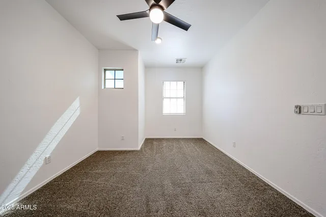 an empty room with a chandelier fan and windows