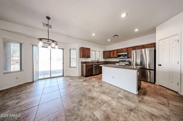 a large kitchen with stainless steel appliances kitchen island granite countertop a refrigerator oven a sink dishwasher and white cabinets with wooden floor