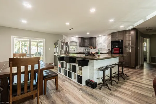 a kitchen with stainless steel appliances kitchen island granite countertop a refrigerator a stove a microwave oven a dining table and chairs with wooden floor