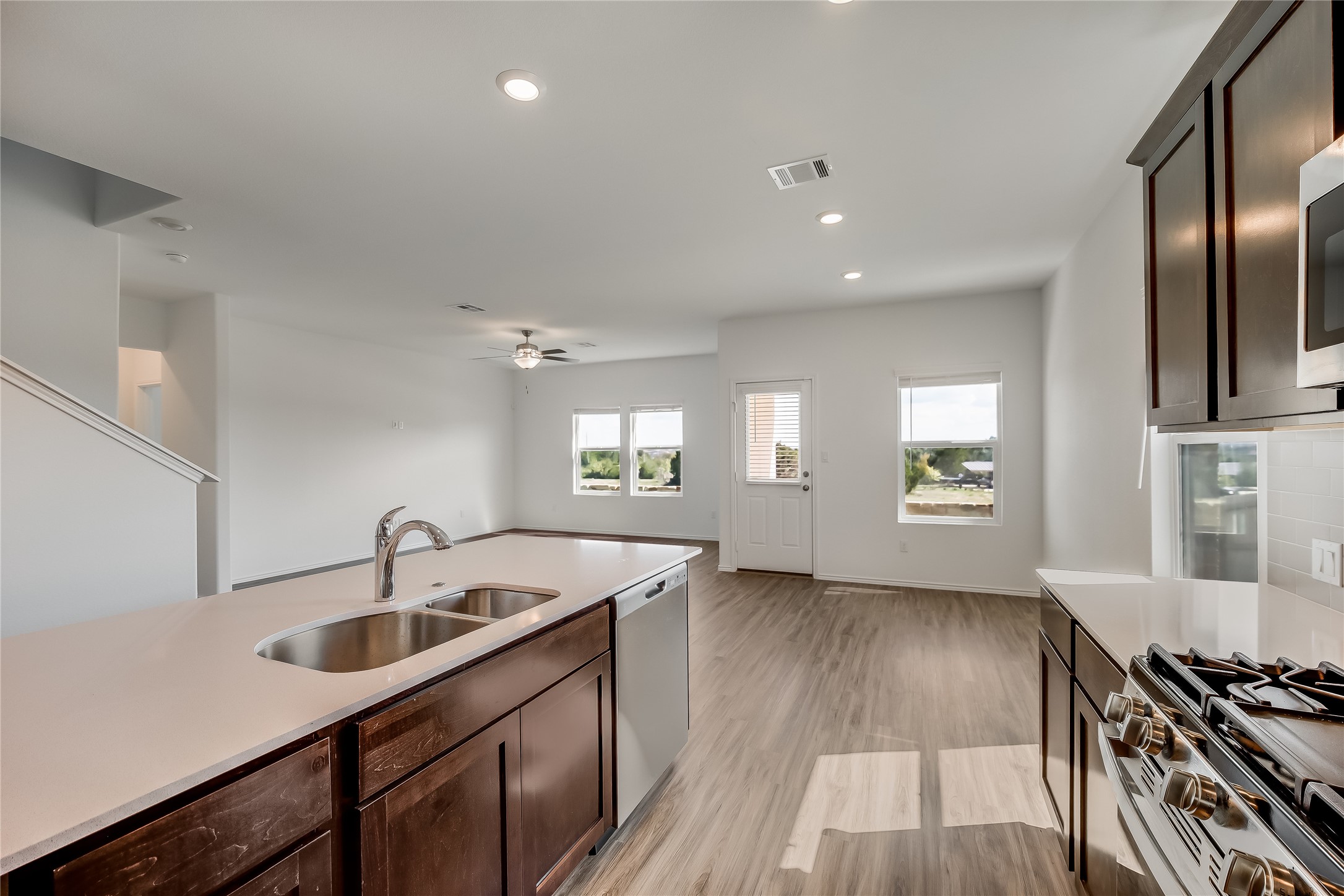 932 Mallow Road Leander, TX 78641 - Photo 7 of 40 Open-concept kitchen featuring an island with a double basin sink, dark wood-finish cabinetry, and light-colored countertops