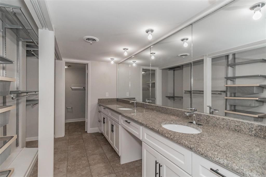 4930 Thunder Road Dallas, TX 75244 - Photo 22 of 23 Expansive dual vanity with a patterned countertop, dual undermount sinks, and white cabinetry with dark hardware