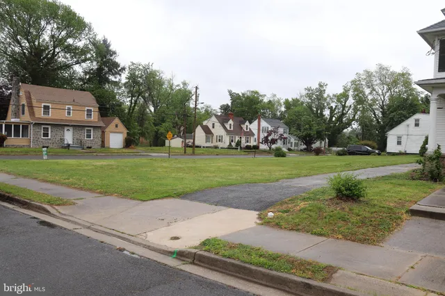 a view of a white house in front of a big yard with plants and large trees