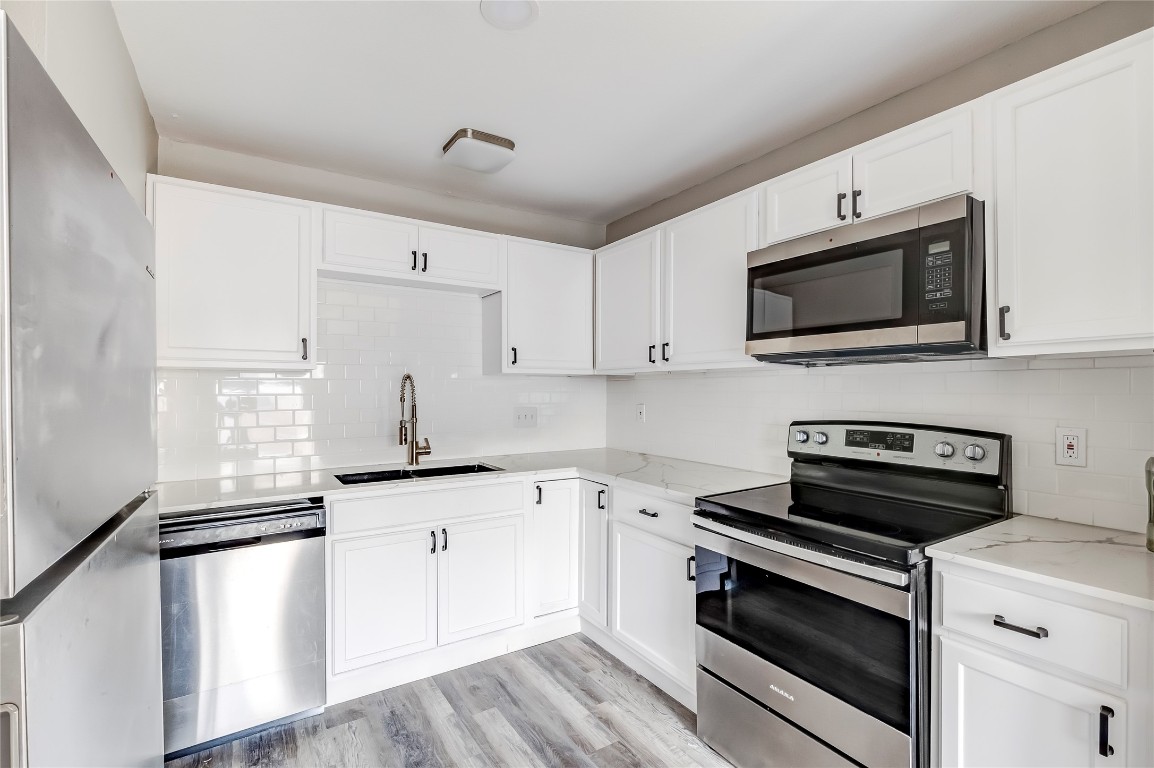 1740 Timber Ridge Road, Unit 136 Austin, TX 78741 - Photo 13 of 32 Kitchen featuring appliances with stainless steel finishes, tasteful backsplash, white cabinetry, and light stone countertops