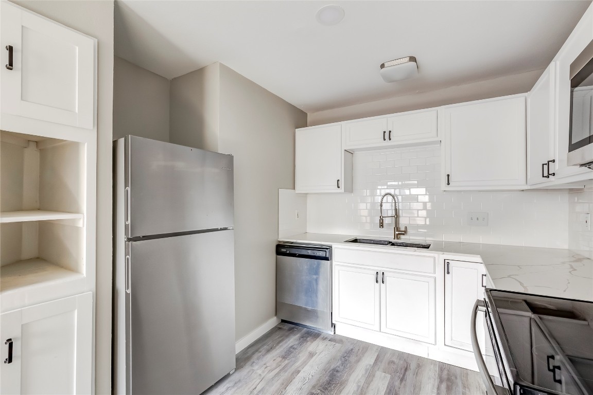 1740 Timber Ridge Road, Unit 136 Austin, TX 78741 - Photo 14 of 32 Kitchen featuring appliances with stainless steel finishes, white cabinets, backsplash, light stone countertops, and light wood finished floors