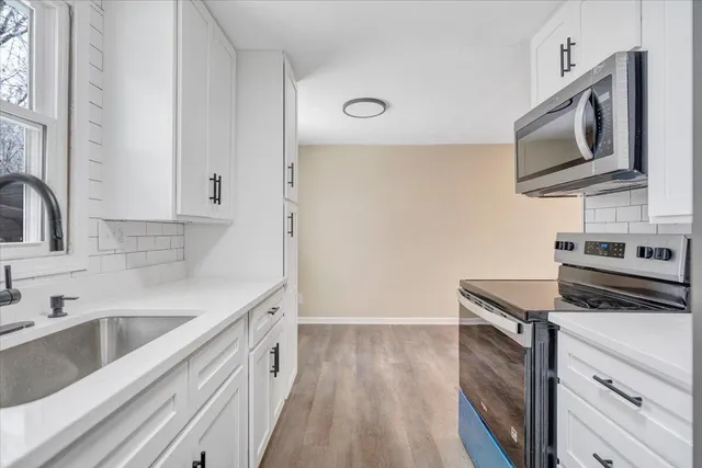 a kitchen with stainless steel appliances white cabinets a sink a stove a microwave and wooden floors