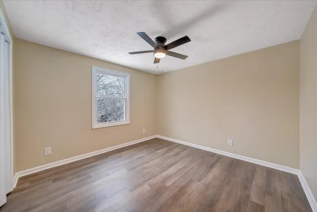 an empty room with wooden floor ceiling fan and window