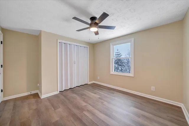 an empty room with wooden floor ceiling fan and windows