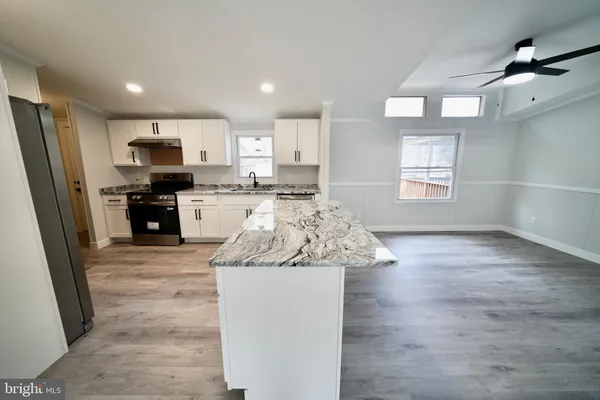 a large kitchen with stainless steel appliances granite countertop a stove a sink a refrigerator white cabinets and wooden floor