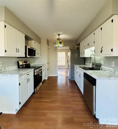 a large kitchen with stainless steel appliances granite countertop a stove top oven a sink and white cabinets