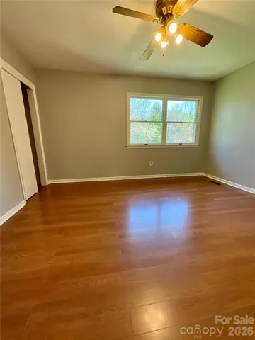 an empty room with wooden floor chandelier fan and windows