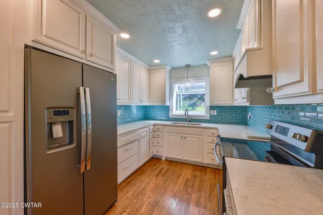 a kitchen with stainless steel appliances granite countertop a refrigerator a sink dishwasher a stove and white countertops with wooden floor