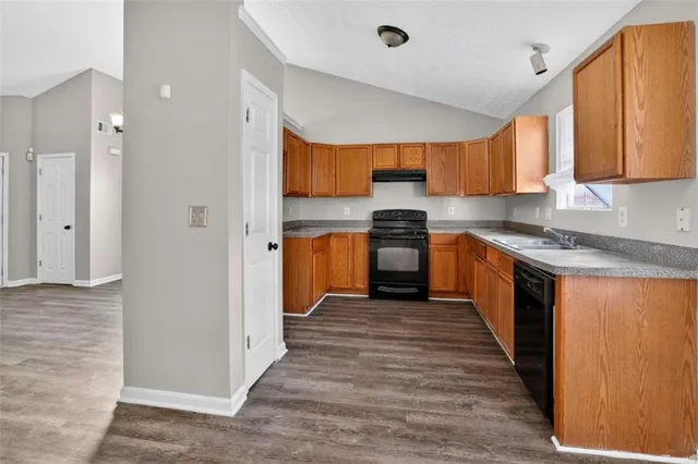 a kitchen with stainless steel appliances granite countertop a stove top oven a sink dishwasher and a refrigerator with wooden floor