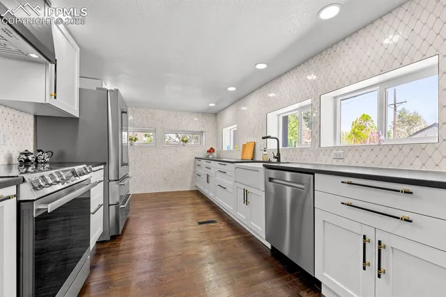 a kitchen with granite countertop a stove top oven a sink dishwasher and white cabinets with wooden floor