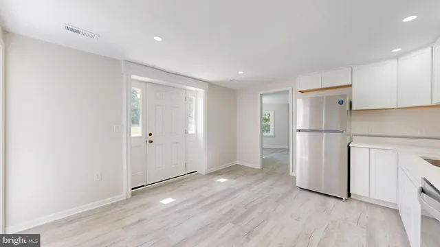 a view of an empty room with wooden floor and a refrigerator