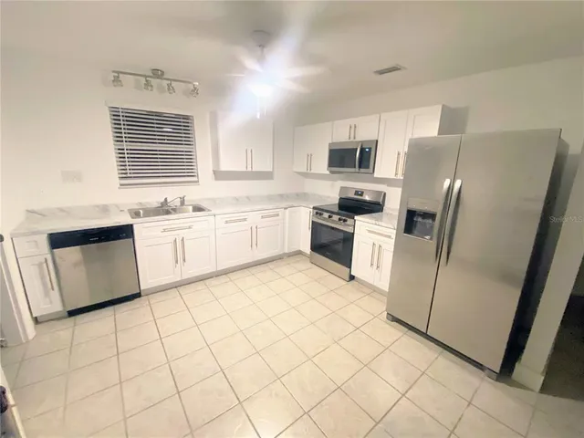 a large kitchen with white cabinets a sink a stove a refrigerator and cabinetry