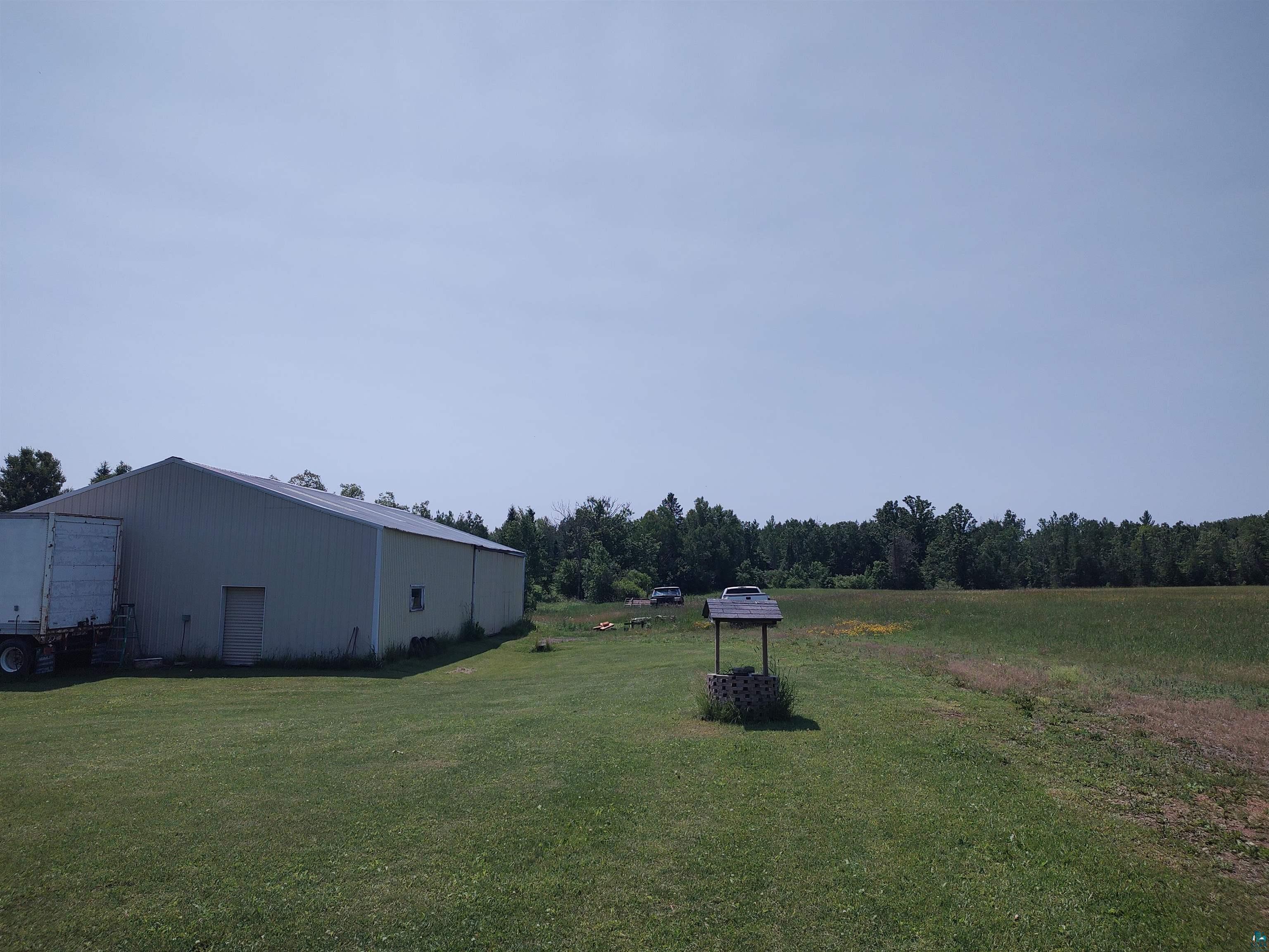 2585 Hautala Road Iron River, WI 54847 - Photo 25 of 28 Large metal-sided utility building with a single personnel door and a window, situated on a substantial grassy lot bordered by mature trees and an open field