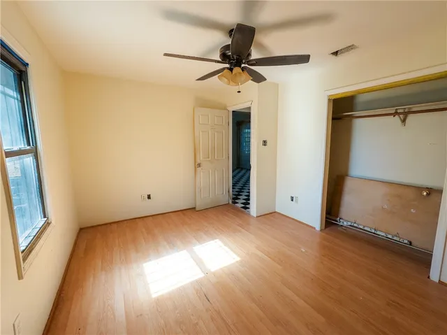 an empty room with wooden floor fan and windows