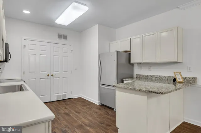 a kitchen that has a refrigerator a sink and white cabinets with wooden floor