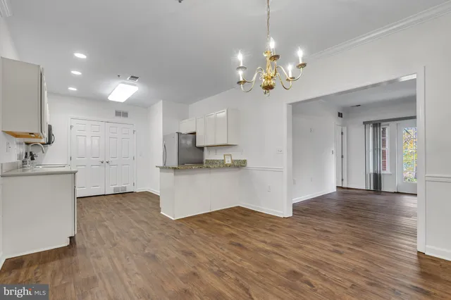 a view of an empty room and kitchen with wooden floor