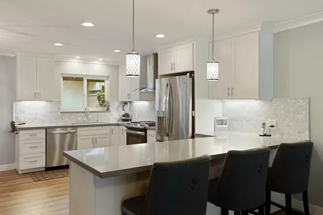 a kitchen with stainless steel appliances granite countertop a refrigerator a sink dishwasher a stove and white cabinets with wooden floor