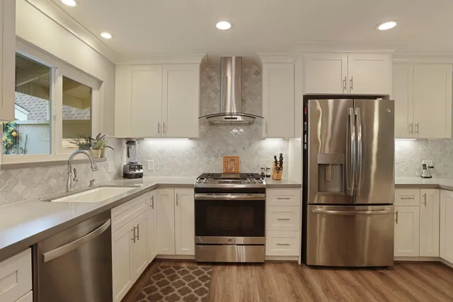 a kitchen with stainless steel appliances granite countertop a stove a sink dishwasher a refrigerator and a fireplace with wooden floor